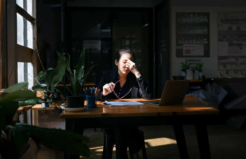 A woman sitting at a desk with a laptop in front of a window, engrossed in her work on an auto draft project.