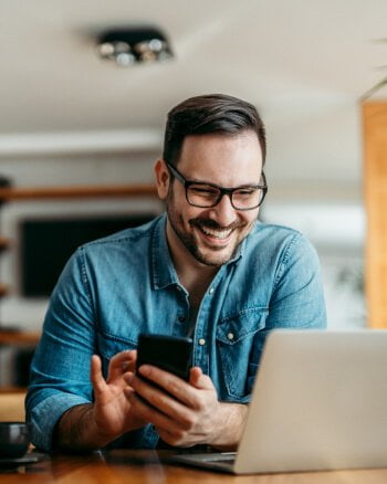 A man is sitting at a table with a laptop and a cup of coffee.