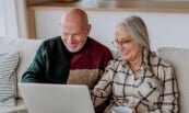 An older couple using a laptop on a couch.